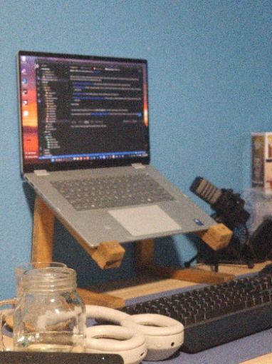 A laptop on
a stand on a desk. There is a microphone and headphones on the desk.